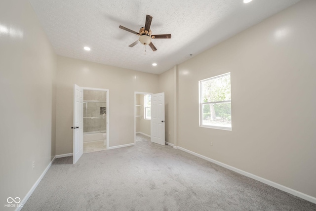 unfurnished bedroom featuring a textured ceiling, baseboards, a spacious closet, carpet, and ensuite bath