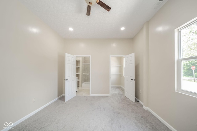 unfurnished bedroom featuring a textured ceiling, connected bathroom, light carpet, baseboards, and a walk in closet