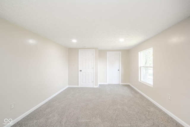 carpeted spare room featuring a textured ceiling and baseboards