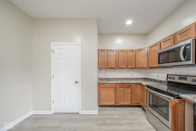 kitchen featuring decorative backsplash, appliances with stainless steel finishes, brown cabinetry, light wood-style floors, and baseboards