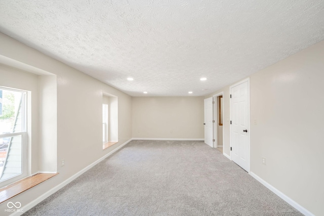 carpeted empty room featuring a textured ceiling, recessed lighting, and baseboards