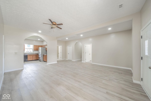 unfurnished living room with arched walkways, recessed lighting, visible vents, light wood-style flooring, and baseboards