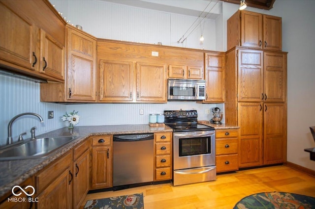 kitchen featuring stainless steel appliances, light wood-style floors, a sink, and brown cabinets