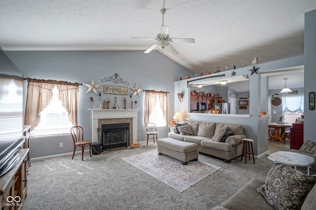 living area with a ceiling fan, lofted ceiling, a tile fireplace, a textured ceiling, and carpet flooring