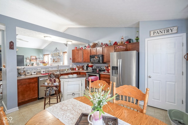 kitchen featuring brown cabinets, a sink, stainless steel appliances, light countertops, and vaulted ceiling