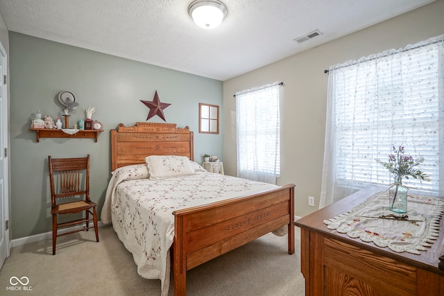 bedroom with visible vents, light colored carpet, and a textured ceiling