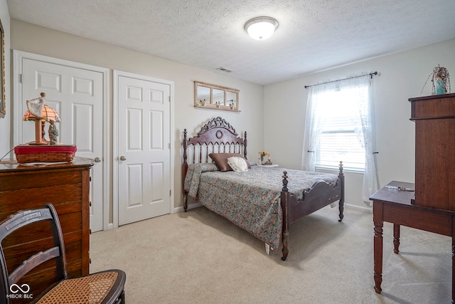 bedroom featuring visible vents, light carpet, a textured ceiling, and baseboards