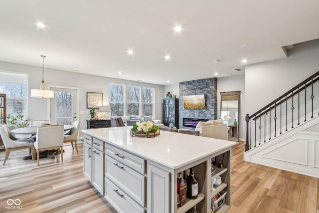 kitchen with a large fireplace, light wood-style flooring, a kitchen island, light countertops, and recessed lighting