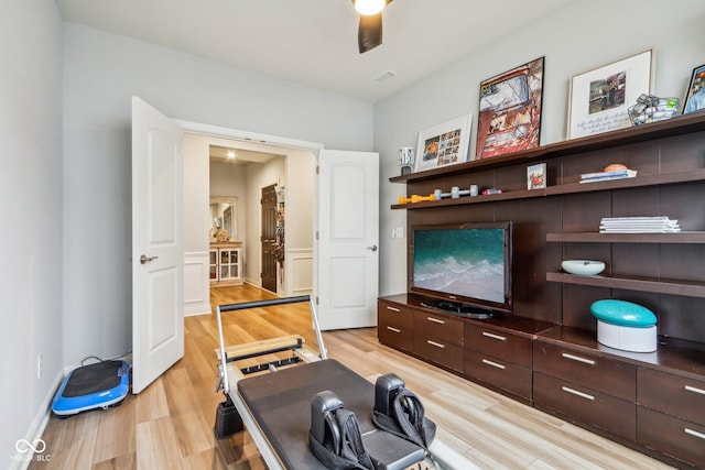 workout room featuring baseboards, visible vents, ceiling fan, and light wood finished floors