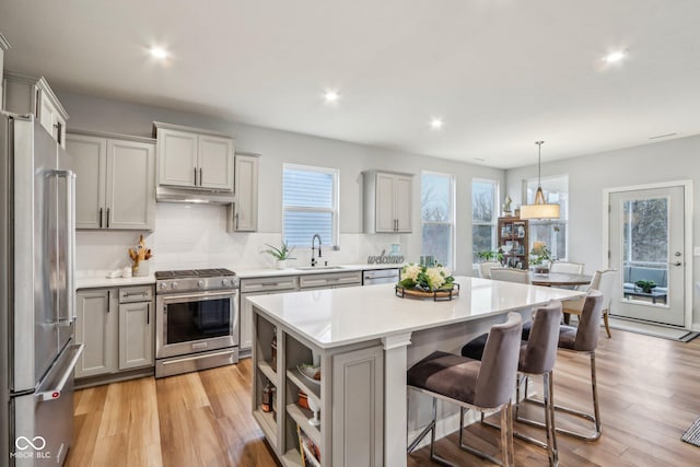 kitchen with a center island, light countertops, appliances with stainless steel finishes, a sink, and under cabinet range hood