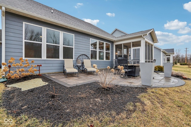 back of property with roof with shingles, a patio area, and a sunroom