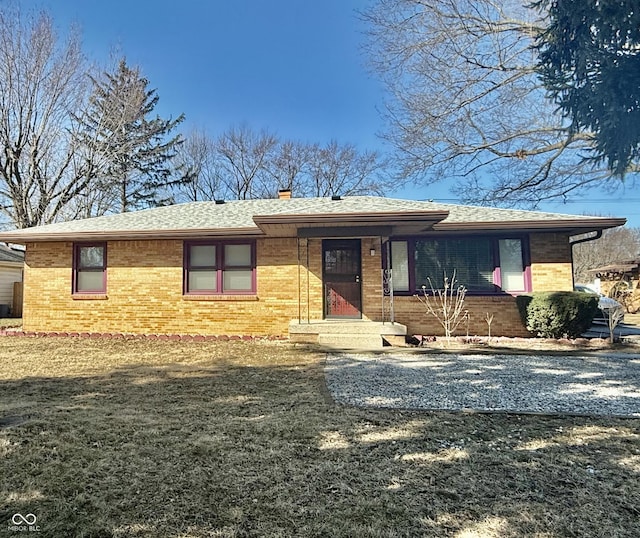 ranch-style home with brick siding, a shingled roof, driveway, a chimney, and a front yard