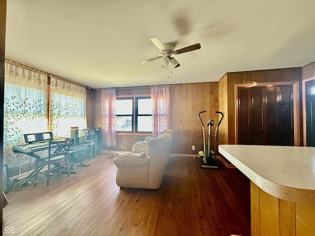 living area with a ceiling fan, wooden walls, and wood finished floors