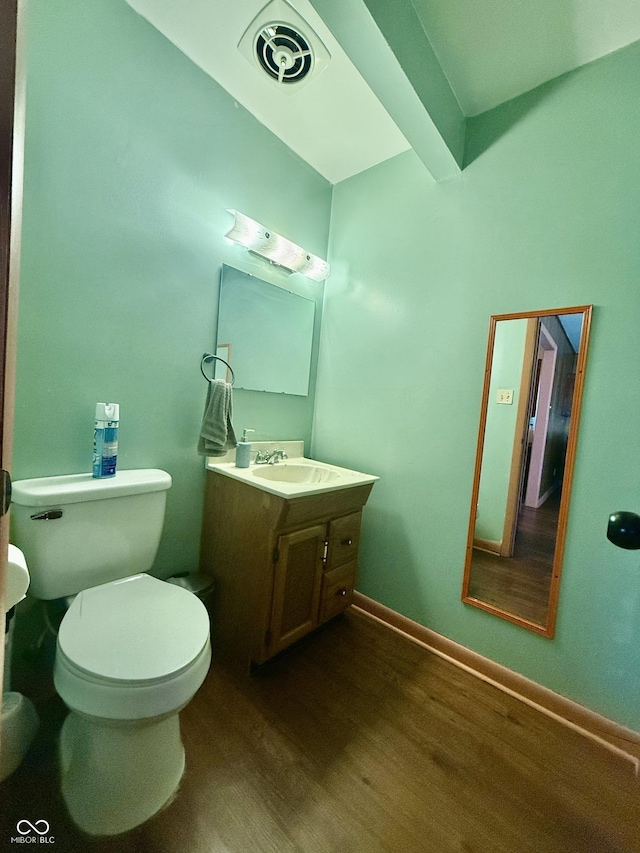 half bathroom with toilet, wood finished floors, vanity, visible vents, and baseboards