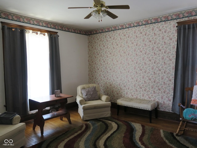 sitting room featuring wood finished floors, ceiling fan, baseboards, and wallpapered walls