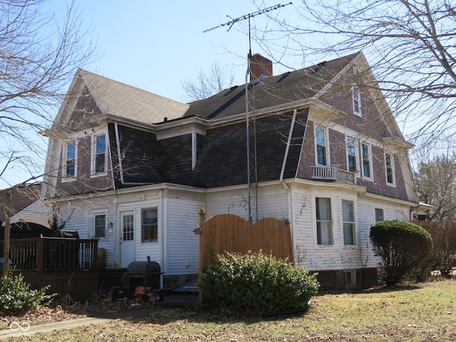 view of side of home featuring a shingled roof, a chimney, and a deck