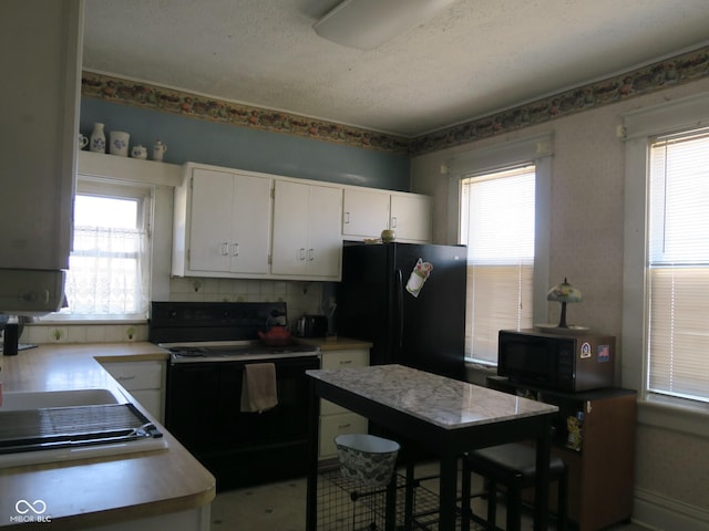 kitchen featuring black appliances, light countertops, a wealth of natural light, and white cabinetry