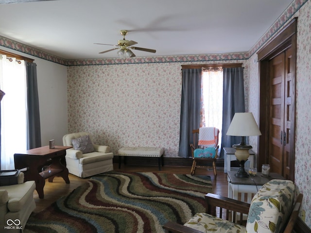 interior space with wood finished floors, a ceiling fan, and wallpapered walls