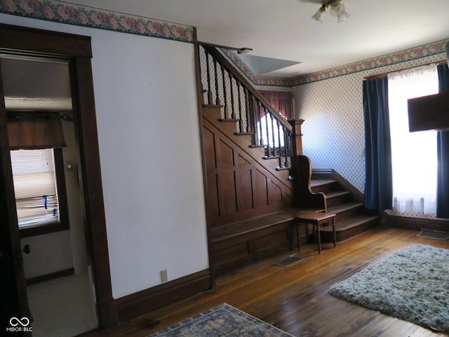 staircase featuring wallpapered walls, baseboards, visible vents, and wood finished floors