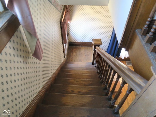 stairs with wood finished floors and wallpapered walls