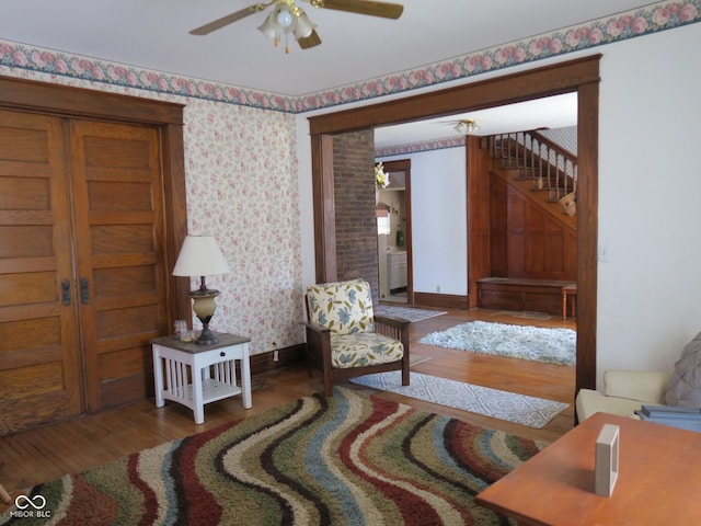 sitting room featuring wallpapered walls, baseboards, stairway, and wood finished floors