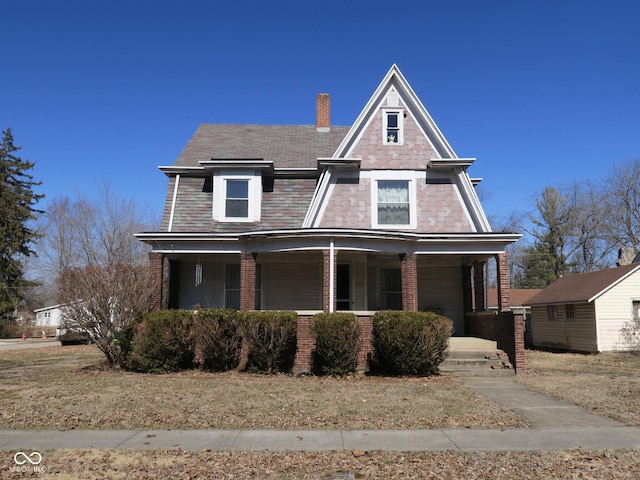 view of front of property featuring a chimney, a porch, and brick siding