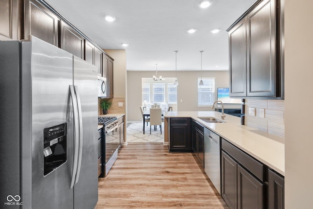 kitchen with pendant lighting, light wood finished floors, stainless steel appliances, light countertops, and a sink