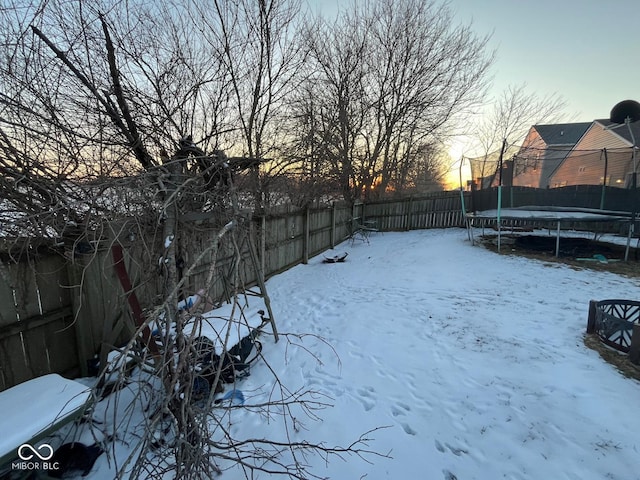 yard layered in snow featuring a trampoline and a fenced backyard