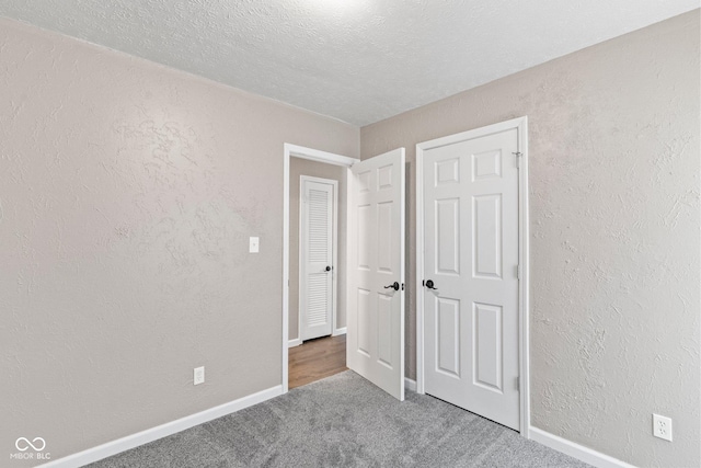 unfurnished bedroom featuring carpet flooring, a textured wall, a textured ceiling, and baseboards