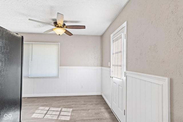 unfurnished room featuring light wood-type flooring, a textured wall, a textured ceiling, and wainscoting