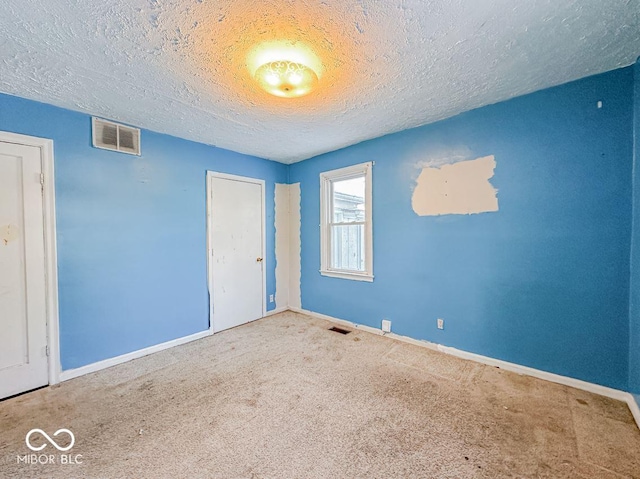 spare room featuring a textured ceiling, carpet, visible vents, and baseboards