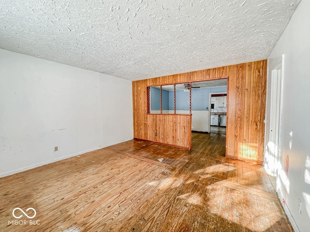 empty room featuring a textured ceiling, wood walls, wood-type flooring, and baseboards