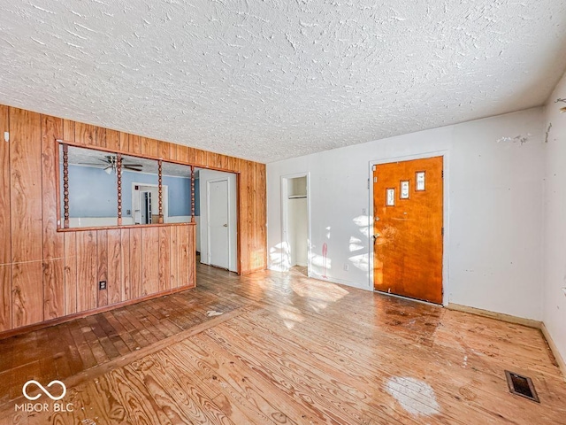 spare room with wooden walls, baseboards, visible vents, wood-type flooring, and a textured ceiling