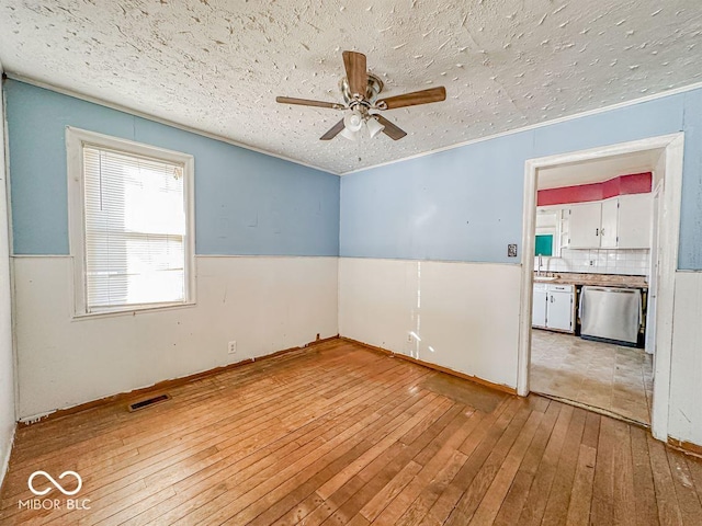 spare room with visible vents, light wood-style flooring, wainscoting, ceiling fan, and a textured ceiling