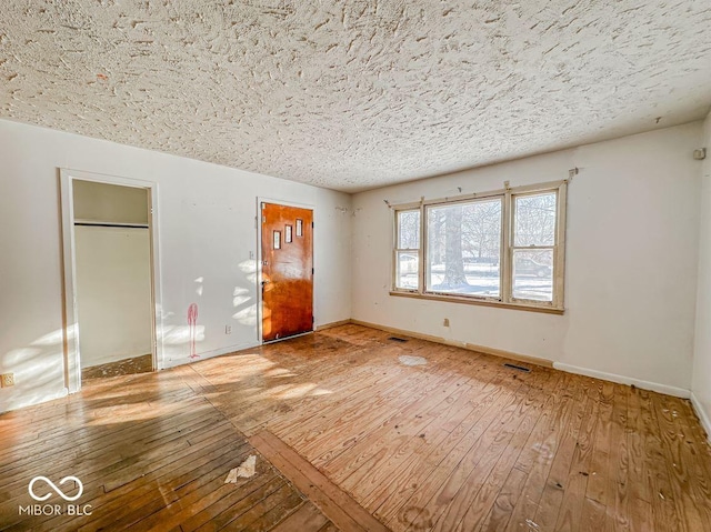 spare room featuring hardwood / wood-style flooring, visible vents, baseboards, and a textured ceiling