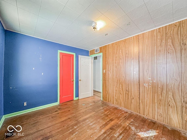 unfurnished room with visible vents, wooden walls, hardwood / wood-style flooring, and baseboards