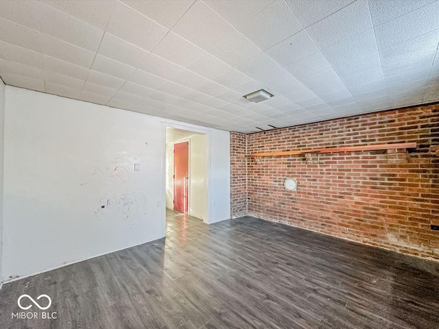 unfurnished room with brick wall and dark wood-style flooring