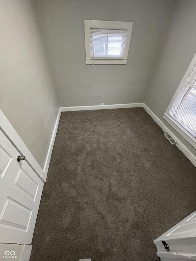 unfurnished room with baseboards and dark carpet