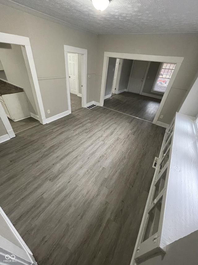 empty room with a textured ceiling, dark wood-style flooring, visible vents, and baseboards