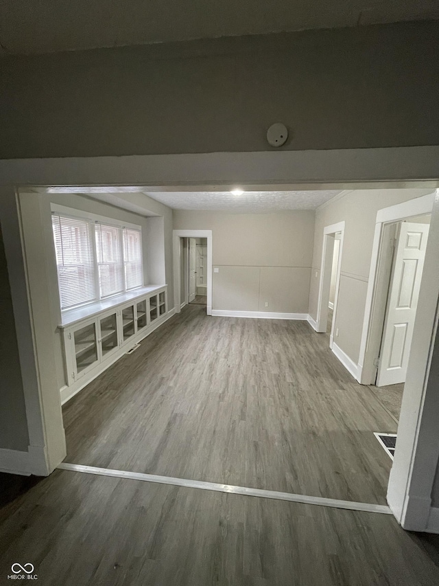 unfurnished room with baseboards, visible vents, wood finished floors, and beamed ceiling