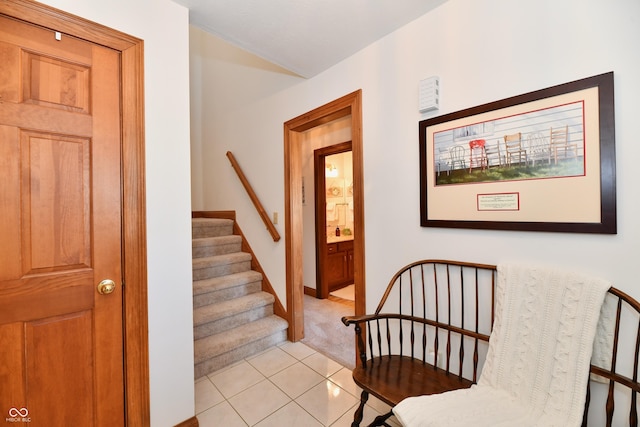 hallway with stairs, light tile patterned flooring, baseboards, and light colored carpet