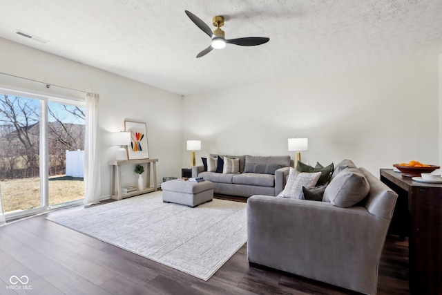 living area with dark wood-style floors, a ceiling fan, visible vents, and a textured ceiling