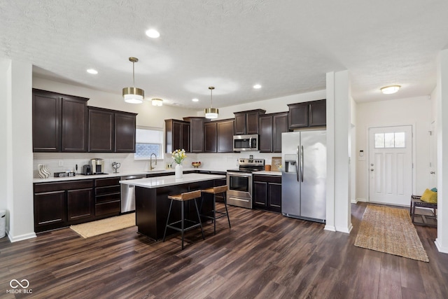 kitchen featuring appliances with stainless steel finishes, dark wood-style flooring, a center island, dark brown cabinets, and a sink