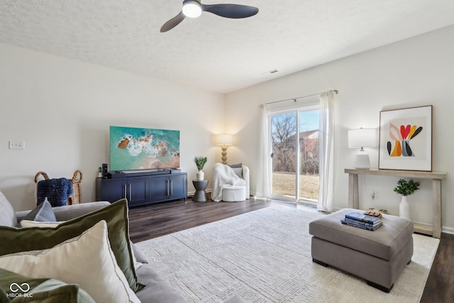 living area featuring ceiling fan, a textured ceiling, baseboards, and wood finished floors