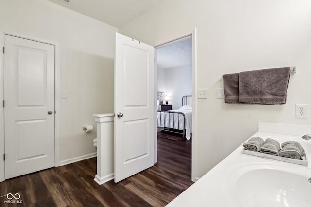 bathroom featuring connected bathroom, toilet, wood finished floors, a sink, and baseboards