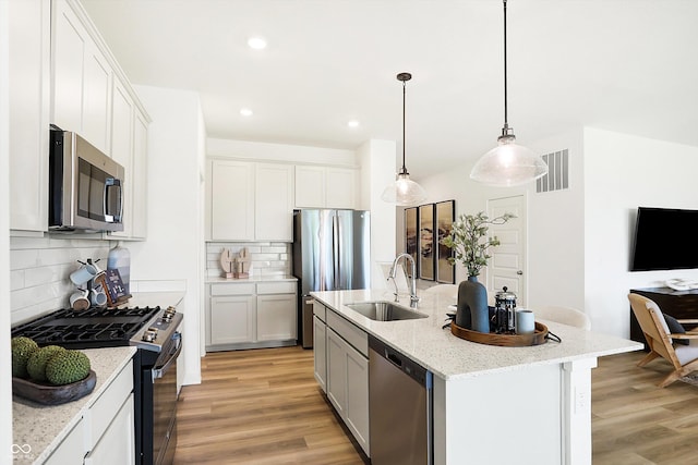 kitchen with light wood-style flooring, stainless steel appliances, a sink, visible vents, and light stone countertops