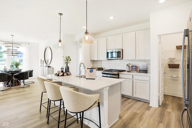 kitchen featuring tasteful backsplash, appliances with stainless steel finishes, white cabinets, a sink, and light wood-type flooring