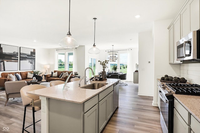 kitchen featuring light wood finished floors, decorative backsplash, open floor plan, stainless steel appliances, and a sink