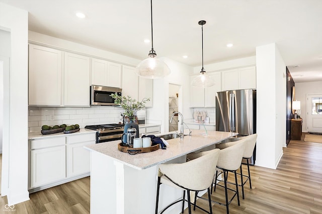 kitchen with appliances with stainless steel finishes, light wood-style floors, a sink, and an island with sink