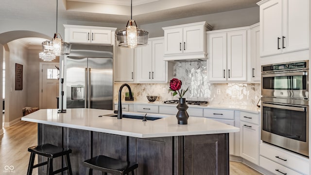 kitchen featuring arched walkways, light wood finished floors, tasteful backsplash, appliances with stainless steel finishes, and a sink